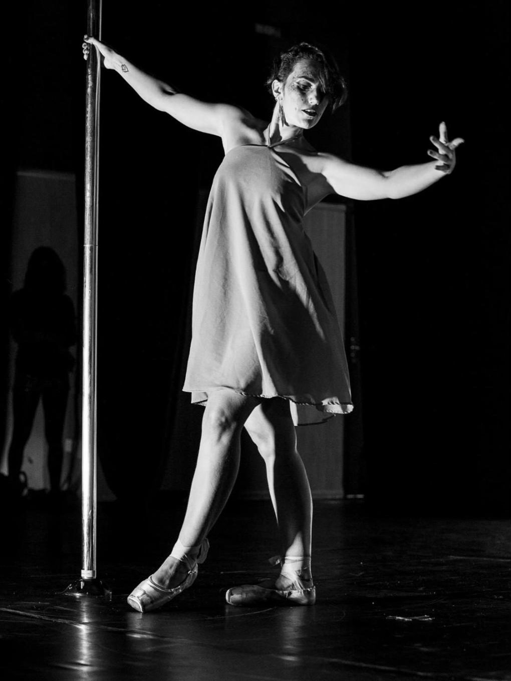 Bailarina com vestido leve e sapatilhas de ponta ao lado do pole, em preto e branco