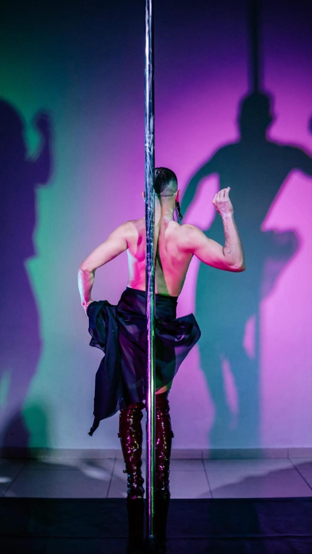 Aluno girando no pole com sombras projetadas na parede rosa